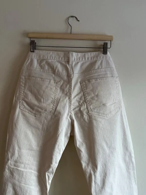 Vita raka jeans med råa kanter - Säljer ett par vita jeans med raka ben och råa, fransiga benslut. Jeansen har klassiska bakfickor och är tillverkade i ett kraftigt bomullstyg. Perfekta för en avslappnad och trendig look.