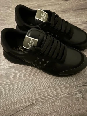 Svarta sneakers från Valentino - Säljer ett par svarta sneakers från Valentino med coola nitar på sidan och breda svarta snören. Skorna har en chunky sula och är gjorda i skinn med detaljer i syntet. Perfekta för dig som gillar en stilren men edgy look.
