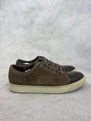 Bruna Lanvin sneakers med lackad tå - Snygga bruna sneakers i mocka med kontrasterande svart, lackad tå och vita sulor. Skorna har klassisk låg profil och matchande bruna skosnören. Perfekta för dig som gillar en stilren men ändå unik look.