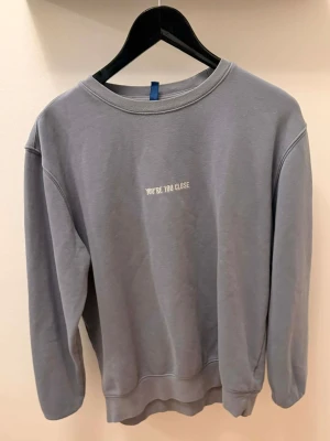 Ljusblå sweatshirt med text - Grå sweatshirt med rund halsringning och vit broderad text 'YOU'RE TOO CLOSE' på bröstet. Tröjan har en avslappnad passform och är tillverkad i mjukt material, perfekt för en chill och stilren look.