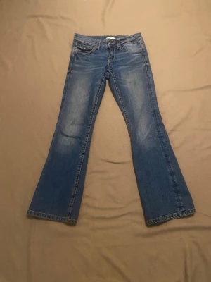 Blå bootcut jeans med fickdetaljer - Snygga blå bootcut jeans med klassisk femficksdesign och coola detaljer på bakfickorna. Jeansen har en lätt tvättad look och utsvängda ben, perfekta för en avslappnad och trendig stil.