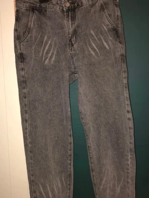 Grå mom jeans med tvättade detaljer - Säljer ett par grå mom jeans med hög midja och tvättade detaljer framtill. Jeansen har raka ben, klassiska fem fickor och knappgylf. Perfekta för en avslappnad och trendig look. Materialet är denim i bomull.
