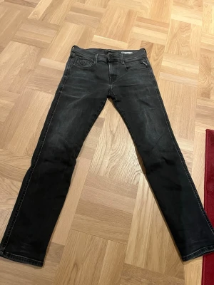 Replay hyperflex anbass - Säljer ett par svarta jeans med rak passform och klassisk femficksdesign. Jeansen har subtila slitningar och är tillverkade i ett mjukt denimtyg som ger en skön känsla. Perfekta för dig som gillar en clean och enkel stil.