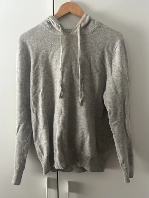 Ljusgrå hoodie med dragsko - En stilren ljusgrå hoodie med huva och dragsko. Tillverkad i mjukt och bekvämt material, perfekt för en avslappnad look. Ribbstickade muddar vid ärmslut och nederkant ger en snygg passform.