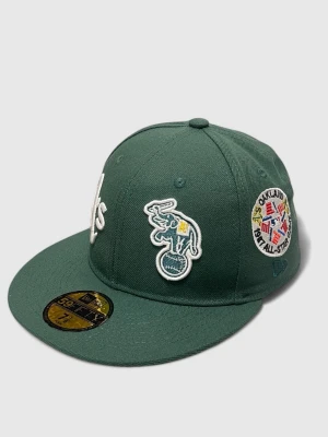 Grön Oakland A's keps New Era 7 1/8 56.8 cm  - Mörkgrön keps från New Era med Oakland A's logga broderad framtill. Kepsen har flera broderade patches på sidorna, bland annat en elefant och texten 'World Series'. Flat skärm och klassisk 59FIFTY-modell.