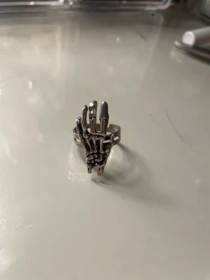 Silvrig ring med skelett-hand - Cool ring i silverfärgad metall med en detaljrik skelett-hand som motiv. Ringen har en öppen design som gör den justerbar och ger en edgy känsla. Perfekt för dig som gillar alternativa accessoarer och vill sticka ut.