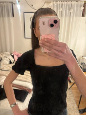 Svart topp med lite puffärm - Snygg svart topp med puffärmar och fyrkantig urringning. Toppens material känns mjukt och lätt,lite ribbad i materialet, perfekt för att lyfta en outfit. Passformen är normal. 