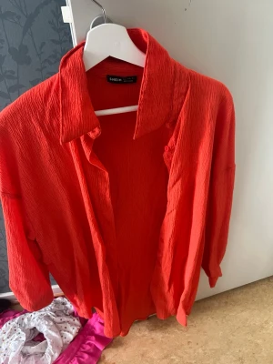 Röd skjorta från SHEIN med struktur - Snygg röd skjorta från SHEIN i ett krinklat, strukturerat tyg. Skjortan har klassisk krage, långa ärmar och en avslappnad passform. Perfekt att styla lager på lager eller bära som den är för en trendig look.