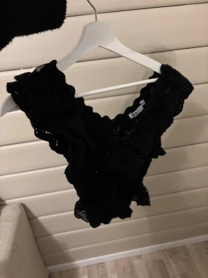 Svart stickad volangtopp - Supersnygg svart topp med djup v-ringning och volangdetaljer. Är i stickat material och är i bra skick