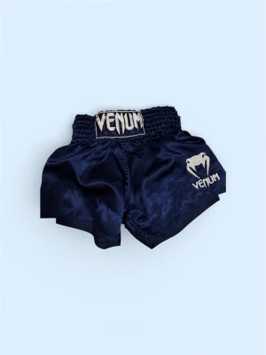 Muaithai shorts från Venum - Snygga mörkblå träningsshorts från Venum med bred resårmidja och broderad logga framtill. Tillverkade i glansigt syntetmaterial som ger en sportig look och är perfekta för kampsport eller gym.