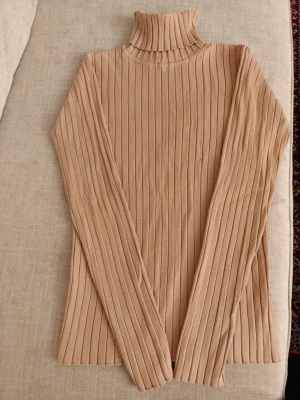 Beige ribbad polotröja från Lindex - Säljer en beige ribbstickad polotröja från Lindex i storlek S. Tröjan har långa ärmar, hög polokrage och är gjord i mjukt stickat material. Perfekt för lager på lager och enkel att matcha med olika outfits.