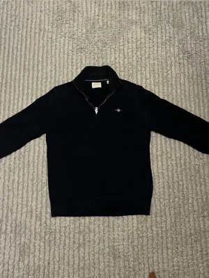 Marinblå zip tröja - Säljer en marin blå zip tröja från Gant, tröjan är rätt så använd och har lite solblekning på delar av axlar och krage. Hör av dig vid funderingar!