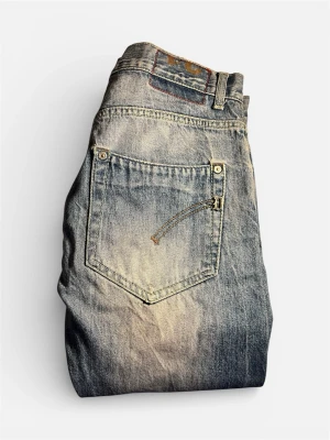 Blå Dondups jeans med vintage-look - Säljer ett par blå jeans med snyggt slitna detaljer och tvättad vintage-look. Jeansen har raka ben, klassisk femficksmodell och knappgylf. Materialet är robust denim i bomull. Perfekta för dig som gillar en avslappnad och trendig stil.