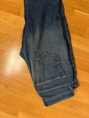 Blå Replay  raka jeans med slitningar  - Säljer ett par blå jeans med raka ben och snygga slitningar framtill. Jeansen har klassisk femficksdesign och kontrastsömmar på bakfickan. Materialet är denim i bomull och de har en avslappnad passform.