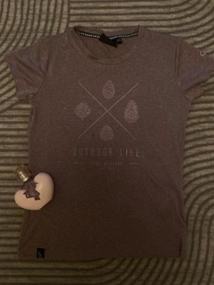 Lila t-shirt från Five Seasons 🧞‍♀️ - Säljer en lila t-shirt från Five Seasons med trycket 'Outdoor Life' och naturinspirerade symboler på bröstet. T-shirten har rund halsringning och korta ärmar. Perfekt för dig som gillar enkel och stilren design. 💜 