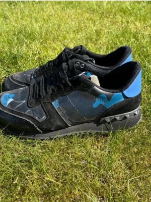 Valentino rock runners - Snygga sneakers i svart och blått med coolt camomönster och nitar på sulan. Skorna har svarta skosnören och detaljer i mocka och läder. Perfekta för dig som vill sticka ut med en unik stil.