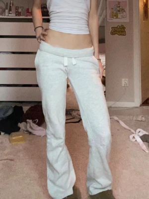 Ljusgrå mjukisbyxor - Liknar Russemerch!! Ljusgrå mjukisbyxor med raka ben och dragsko i midjan. Byxorna har två bakfickor med broderad detalj och är gjorda i mjukt, stretchigt material. Perfekta för en chill och avslappnad stil. Be bild för att se lagning på baksidan!