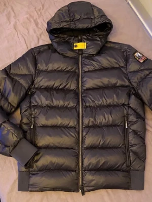  Parajumpers SHEEN - Snygg svart pufferjacka från Parajumpers med huva och gul detalj vid halsen. Jackan har två dragkedjeförsedda fickor, ribbade muddar och klassisk patch på ärmen. Perfekt för kalla dagar och riktigt varm tack vare det vadderade materialet.  Äkta vara. Byter också gärna med en canada goose Wyndham