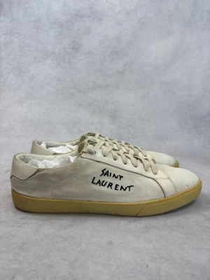 Saint Laurent vita sneakers - Snygga vita sneakers från Saint Laurent i canvas med handskriven logga på sidan. Skorna har beige gummisula och matchande vita skosnören. Klassisk låg modell som passar till det mesta och ger en clean look.