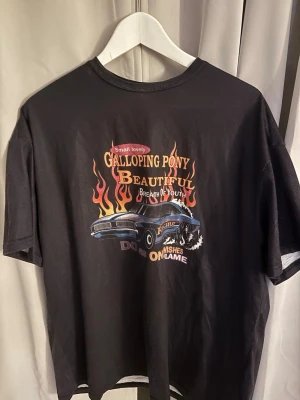 Svart t-shirt med biltryck och flames - Svart t-shirt med färgglatt tryck framtill.  T-shirten har rund hals och korta ärmar och är lite oversize från SHEIN i storlek M