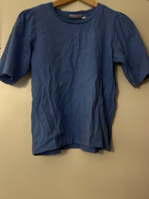 Blå t-shirt med puffärmar - Snygg blå t-shirt med puffärmar och rund halsringning.