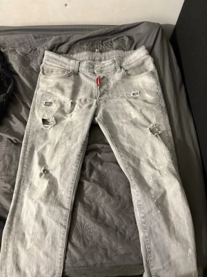 Ljusa slitna jeans från Dsquared2 - Säljer ett par ljusgrå jeans från Dsquared2 med distressed detaljer och hål på benen. Jeansen har knappgylf och klassisk femficksmodell. Perfekta för dig som gillar en edgy och trendig stil. 
