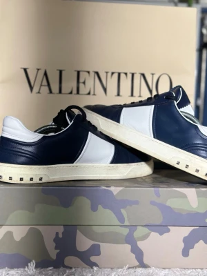 Marinblå valentino flycrews - Snygga sneakers från Valentino i marinblått och vitt. Skorna har klassisk låg profil, vita detaljer på sidan och små nitar på sulan. Tillverkade i skinn med vita snören och en stilren design som sticker ut. Utan innersula!