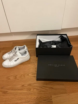 Vita Philipp Plein sneakers i läder - Stilrena vita sneakers från Philipp Plein i äkta kalv läder  med vita skosnören och logga på sidan. Skorna är köpta från farfetch helt nya. Nypris ligger runt 5500kr. Skorna är använda hyfsat lite men har tappat färgen på vissa ställen på skorna. Box, kvitto och dustbag finns, skriv vid minsta fundering eller fråga!