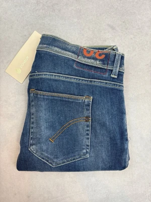 Blå raka jeans från Dondup - Snygga blå jeans från Dondup med raka ben och klassisk femficksdesign. Jeansen har en lätt tvättad look med slitningar och kontrastsömmar. Tillverkade i mjukt denimtyg som ger en skön passform. Perfekta för en avslappnad och trendig stil.