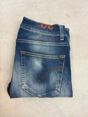 Blå slitna jeans från Dondup - Säljer ett par blå jeans från Dondup med slitningar och distressed detaljer. Jeansen har klassisk femficksmodell, raka ben och snygga kontrastsömmar. Materialet är denim i bomull och de har en cool tvättad look med ljusa partier.