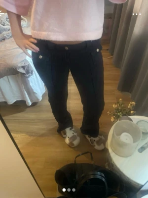 Svarta jeans med knappar - Säljer ett par svarta jeans med raka ben och dekorativa silverfärgade knappar vid fickorna. Jeansen har låg midja och klassisk femficksdesign. Perfekta för en avslappnad och trendig look.
