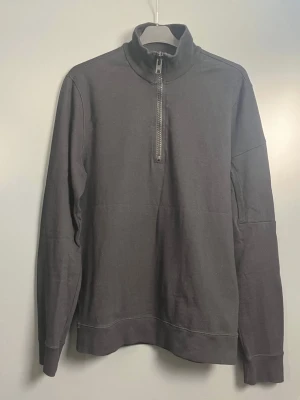 Peak Performance - Snygg svart långärmad tröja från Peak Performance med hög krage och dragkedja framtill. Tillverkad i mjukt bomullsmaterial, perfekt för en avslappnad och sportig stil. Klassisk och enkel design som funkar till det mesta.