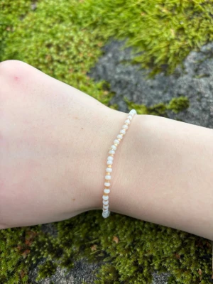 Vitt pärlarmband med små pärlor - Sött armband med små vita pärlor trädda på elastisk tråd. Armbandet är enkelt och stilrent, perfekt för dig som gillar minimalistiska accessoarer. Passar att bära ensamt eller tillsammans med andra armband för en personlig look.