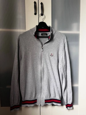 Moncler Cardigan - En riktigt snygg grå Moncler cardigan i toppskick. Klassisk och tidlös design som funkar till både vardag och mer uppklädda outfits. Mjuk och skön kvalitet med perfekt passform. Storlek XL men passar L. 