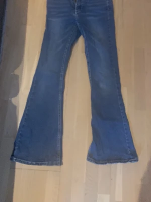 Blå utsvängda jeans med hög midja - Säljer ett par blå jeans med utsvängda ben och hög midja. Klassisk femficksmodell och snygg tvätt som passar till det mesta. Perfekta för dig som gillar retrovibbar och vill ha ett par jeans som sticker ut lite extra.