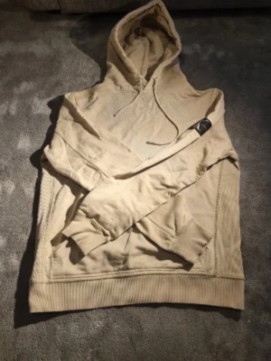 Beige hoodie från Calvin Klein Jeans - Snygg beige hoodie från Calvin Klein Jeans med klassisk huva och dragsko. Tillverkad i mjuk bomull och har ribbade muddar vid ärmslut och nederkant. Perfekt för en chill och stilren look. ✅