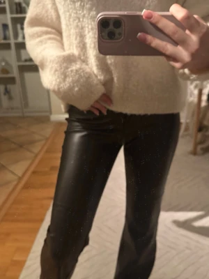 Svarta PU-byxor med utsvängda ben - Säljer ett par svarta PU-byxor från Nelly med låg midja och utsvängda ben. Byxorna har en snygg glansig finish och stängs med knapp och dragkedja. Perfekta för dig som vill ha en trendig och edgy look.