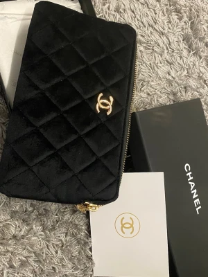 Svart quiltad plånbok från Chanel - Lyxig svart plånbok från Chanel med klassiskt quiltat mönster och guldfärgat CC-logo framtill. Plånboken har dragkedja och är tillverkad i läder, perfekt för dig som gillar exklusiva accessoarer med tidlös design.