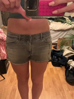 Grå denimshorts med rå kant - Snygga grå denimshorts med rå kant nertill och klassisk femficksdesign. Shortsen har låg midja och en avslappnad passform, perfekta för varma dagar. Ingen synlig logga eller märke på shortsen.