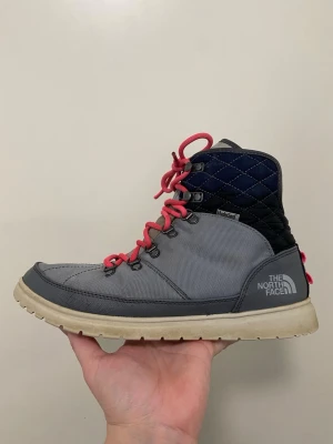 Grå kängor från The North Face - Snygga grå kängor från The North Face. Fodrade. Yttermaterialet är slitstarkt textil och sulan är beige och rejäl för bra grepp. Varma och sköna. Tål snö och slask. Vind- och vattenavvisande. Tyvärr har dem mindre slitage iform av sprickor, se sista bild. Läcker inte in.