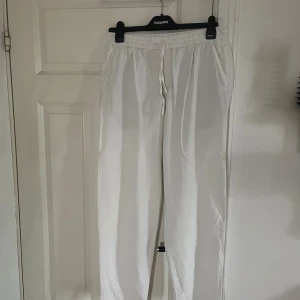 Vita linnebyxor med resårmidja - Säljer ett par vita linnebyxor från KappAhl med avslappnad passform och resår i midjan. Byxorna har snörning framtill, sidofickor och två dekorativa bakfickor. Perfekta för en chill och stilren look.