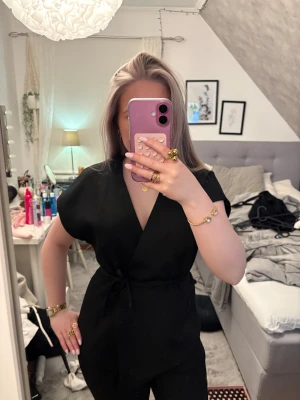 Svart omlott topp med knytband - Säljer en svart omlottopp med knyt i midjan och korta ärmar. Toppen har en v-ringad design och är enkel men stilren, perfekt att matcha med jeans eller kjol. 