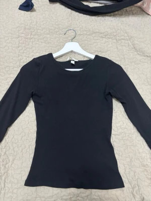 Svart ribbad långärmad topp - En enkel och stilren svart ribbad topp med lång ärm och rund halsringning. Perfekt basplagg som passar till det mesta och har en slim passform. Tillverkad i mjukt material för skön känsla.