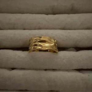 Slumpmässig ring på köpet ❣️ - Snygg bred ring i guldfärgad metall med unik vågig och abstrakt design. Ringen har en modern look med flera lager som ger en cool och trendig känsla. Perfekt för dig som vill sticka ut med dina accessoarer.
