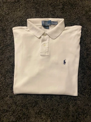 Vit Ralph lauren piké - Vit pikéskjorta från Polo Ralph Lauren med klassisk krage och två knappar framtill. Skjortan har en broderad marinblå logga på bröstet och är tillverkad i mjuk bomull för en clean och stilren look.