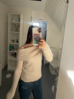 Off shoulder beige stickad tröja - Mysig off shoulder stickad tröja i beige med bred ribbad kant upptill. Tröjan har lång ärm och en mjuk, fluffig känsla som ger en avslappnad men ändå trendig look. Perfekt att matcha med jeans för en enkel och snygg outfit. Den är i strl 134-140 men jag som är en S kan ha den men blir lite liten så en strl större än 140 funkar