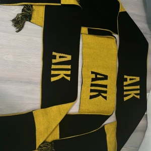 AIK halsduk i svart och gult - Säljer alla 3 för 180 Snygg halsduk i AIK:s klassiska färger svart och gult med tydlig AIK-logga på båda sidor. Halsduken har fransar i ändarna och är perfekt för att visa ditt stöd på matchen. Tjockt och mjukt material som håller dig varm på läktaren.
