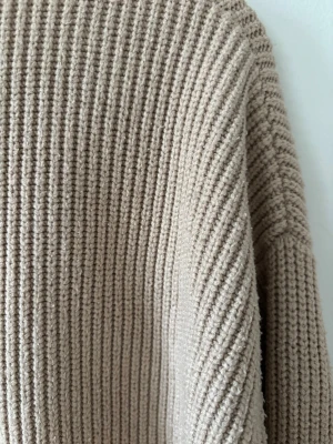 Beige ribbstickad tröja - En beige ribbstickad tröja med avslappnad passform och långa ärmar. Tröjan har en rak, något boxig siluett och är tillverkad i ett mjukt, tjockare garn som ger en mysig känsla. Perfekt för lager-på-lager och enkel att matcha med olika outfits. Väldigt skön material. 