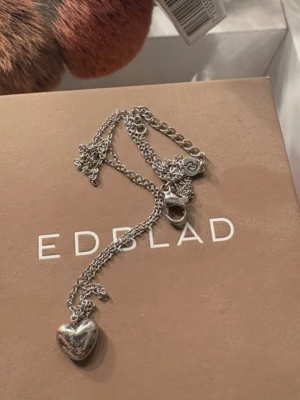 Silverhalsband med hjärthänge Edblad - Snyggt halsband i silverfärgad metall från Edblad med ett blankt hjärthänge. Kedjan är tunn och har ett klassiskt lås. Perfekt accessoar för att lyfta din outfit med en stilren och romantisk touch.