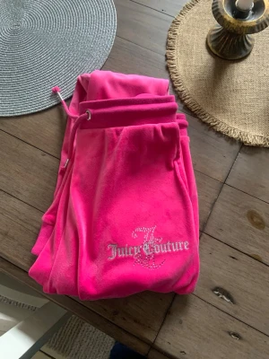 Juicy Couture rosa velourbyxor - Säljer ett par ikoniska rosa mjukisbyxor från Juicy Couture i mjuk velour. Byxorna har dragsko i midjan och glittrig Juicy Couture-logga med strassdetaljer på benet. Perfekta för en chill och trendig look.pris kan diskuteras storlek 170, skulle nästan säga xs